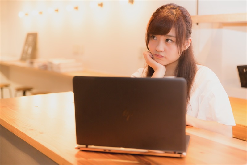 ノートパソコンの前で考え事をする女性